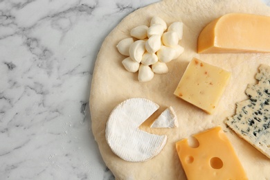 Photo of Pizza crust with fresh ingredients on marble table, top view