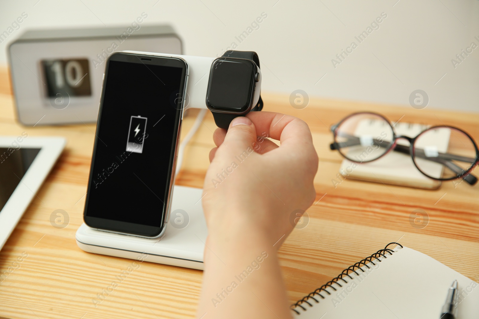 Photo of Man putting smartwatch onto wireless charger at wooden table, closeup. Modern workplace accessory