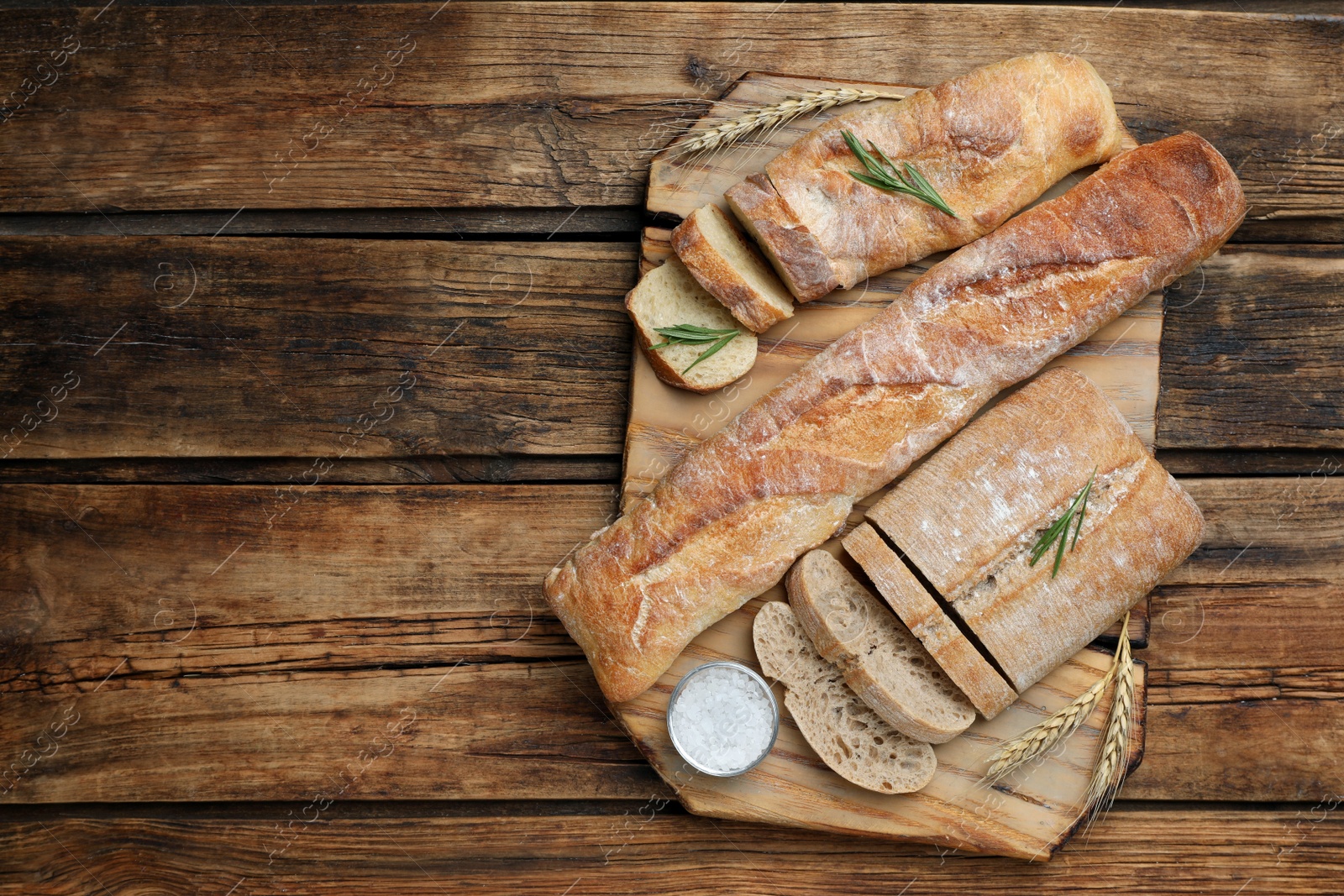 Photo of Cut fresh ciabatta and baguettes on wooden table, top view. Space for text