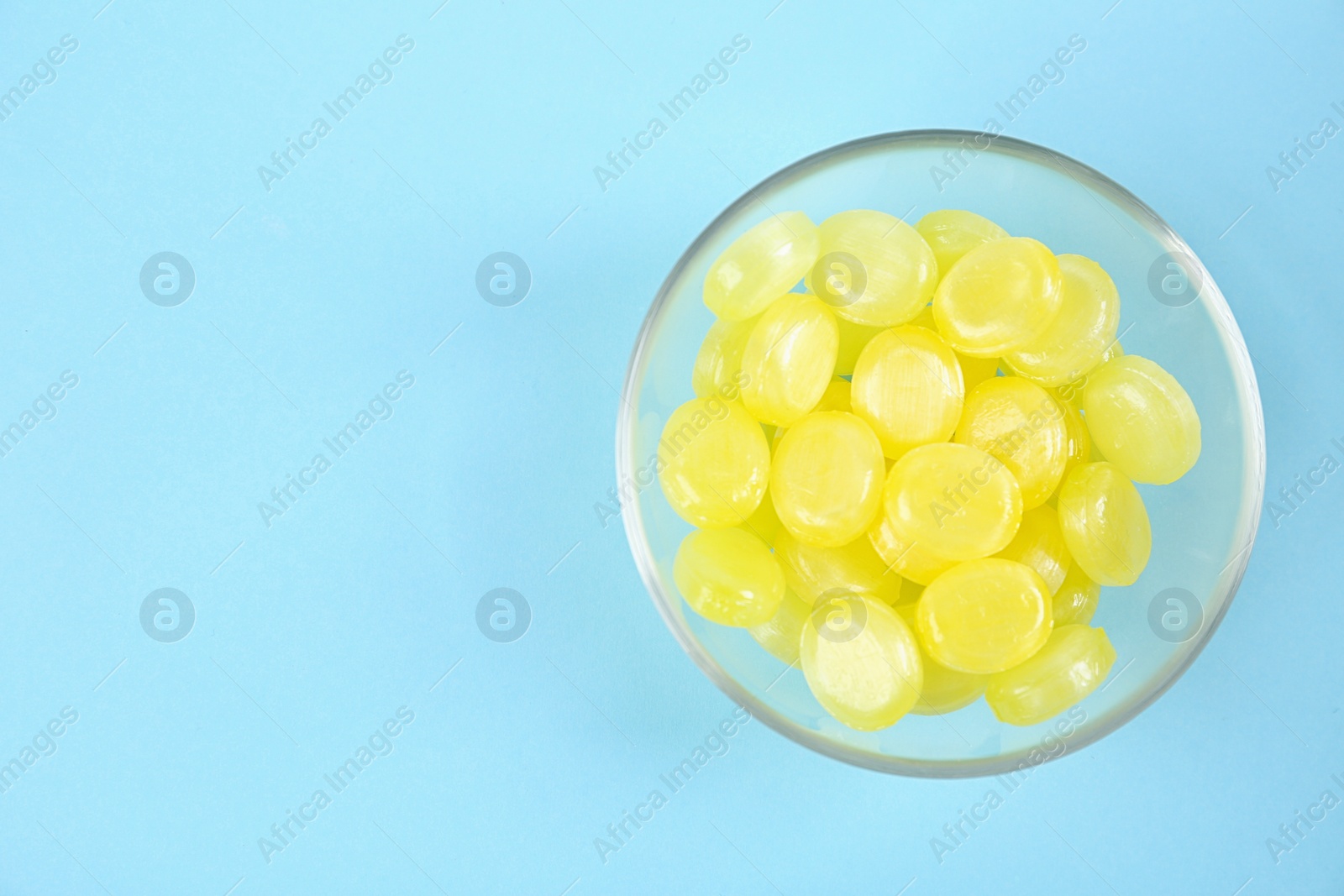 Photo of Delicious lemon drops in bowl on light blue background, top view. Space for text