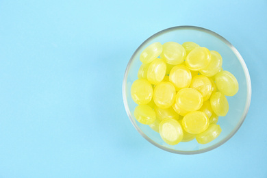 Photo of Delicious lemon drops in bowl on light blue background, top view. Space for text