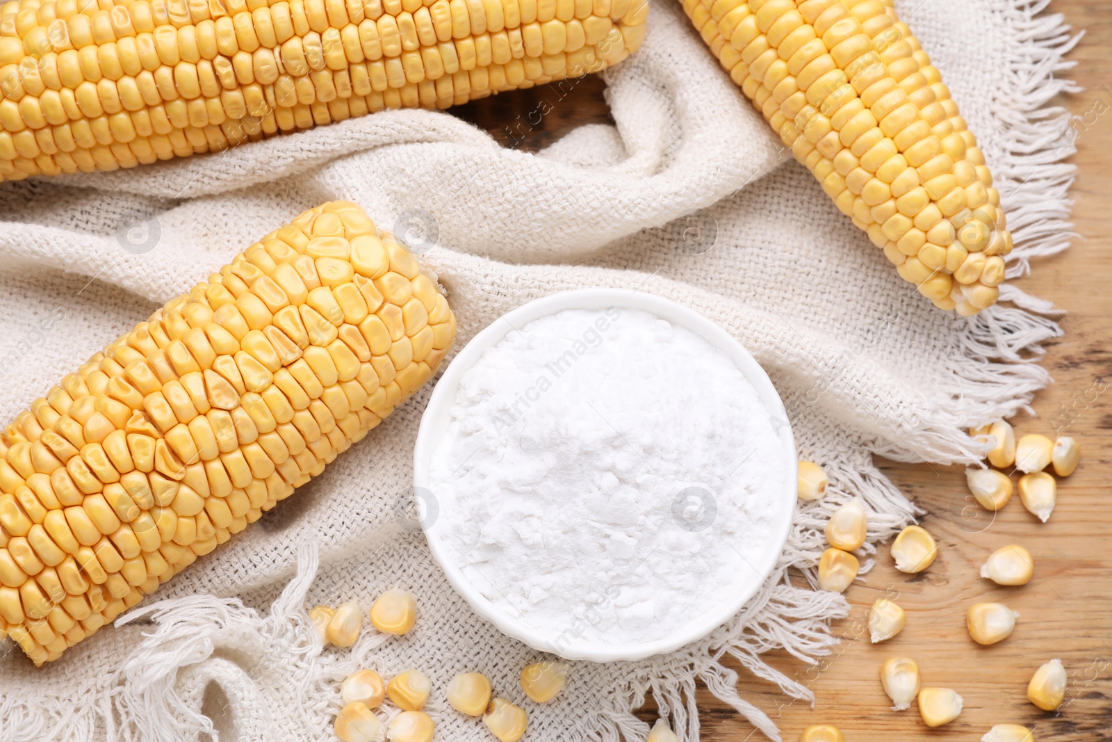 Photo of Bowl with corn starch, ripe cobs and kernels on wooden table, flat lay