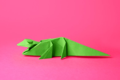 Photo of Origami art. Handmade green paper crocodile on pink background