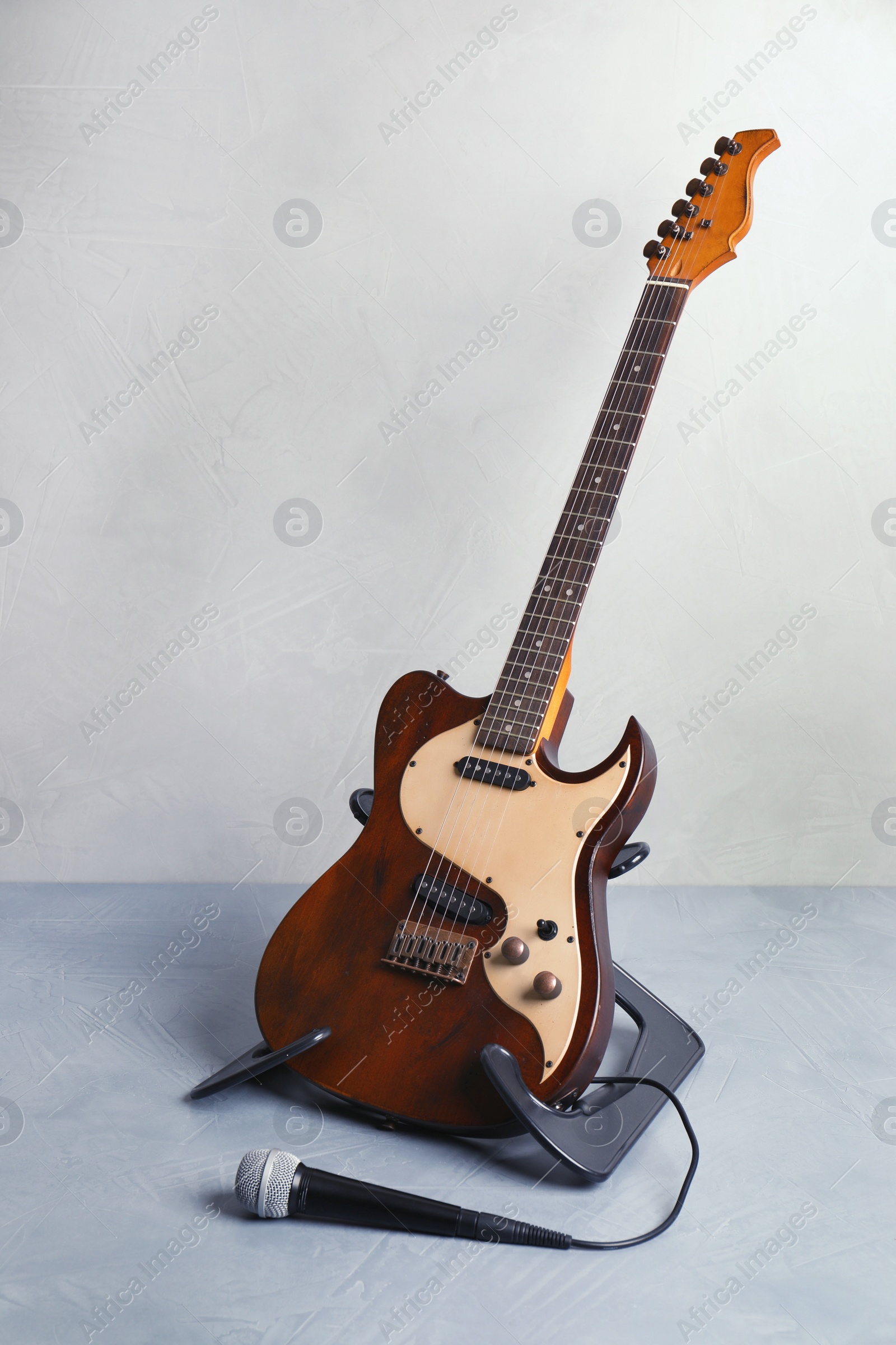Photo of Stand with modern electric guitar and microphone on floor near color wall