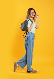 Happy woman with backpack on yellow background