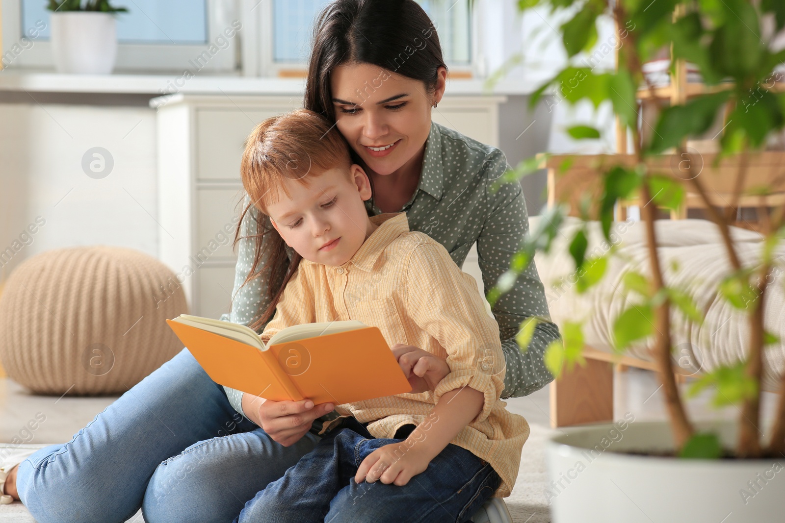 Photo of Mother reading book with her son on floor in living room at home