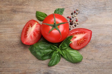 Fresh green basil leaves, spices with cut and whole 
tomatoes on wooden table, flat lay