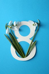 Photo of Beautiful snowdrops and paper number 8 on light blue background, flat lay