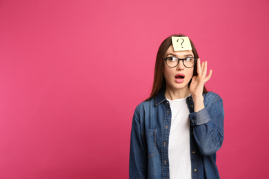 Photo of Emotional woman with question mark sticker on forehead against pink background. Space for text