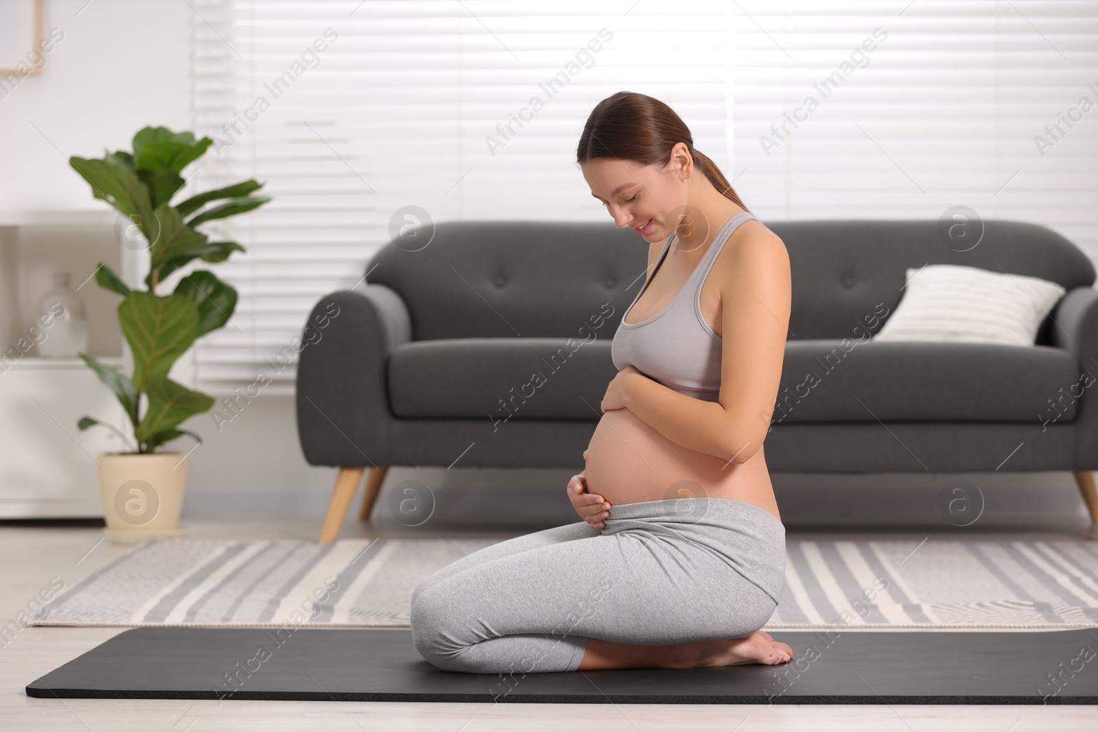 Photo of Pregnant woman sitting on yoga mat at home