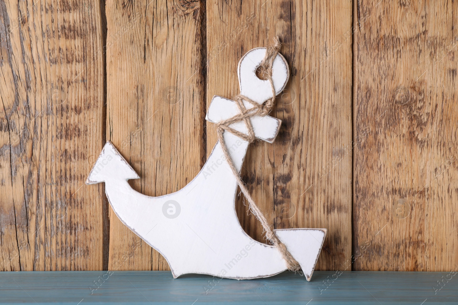 Photo of Anchor with hemp rope on light blue table near wooden wall