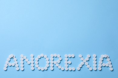 Photo of Word Anorexia made of white pills on light blue background, flat lay. Space for text
