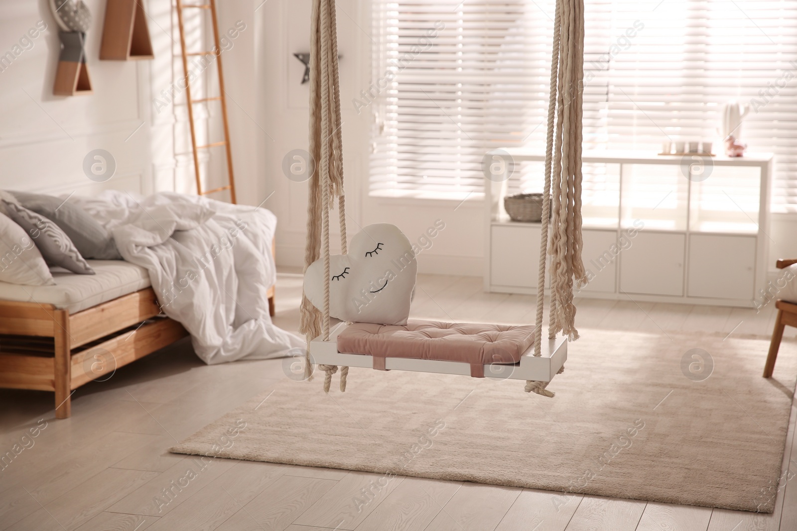 Photo of Beautiful swing with toy heart in bedroom. Stylish interior design