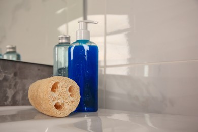 Photo of Natural loofah sponge and shower gel bottles on washbasin in bathroom, space for text
