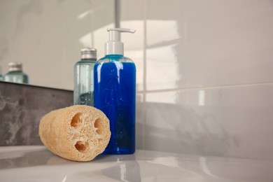 Natural loofah sponge and shower gel bottles on washbasin in bathroom, space for text