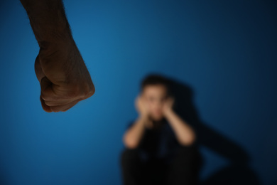 Photo of Man threatens his son on blue background, focus on hand. Domestic violence concept