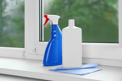 Photo of Bottles of cleaning products and dustrag on windowsill