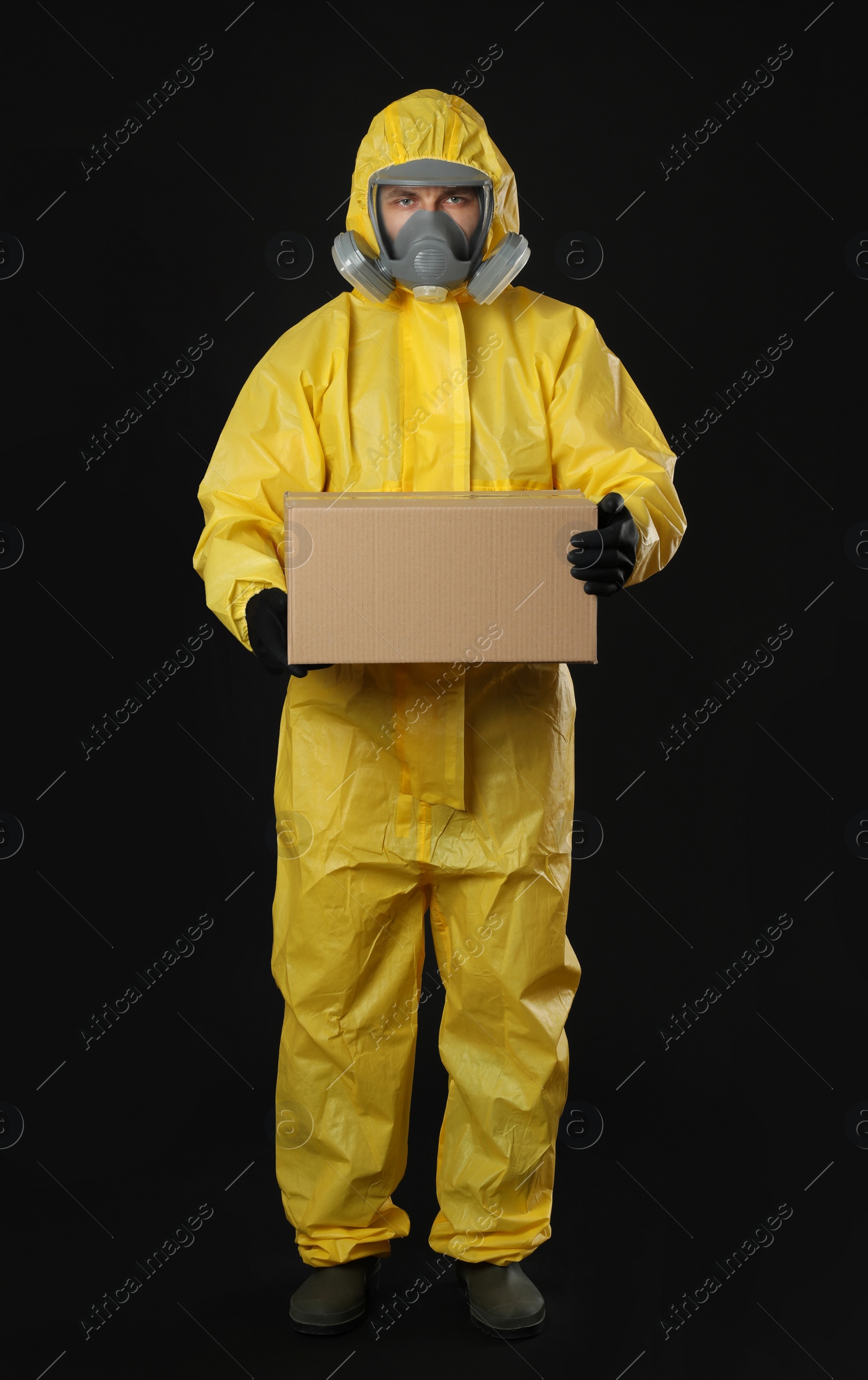 Photo of Man wearing chemical protective suit with cardboard box on black background. Prevention of virus spread