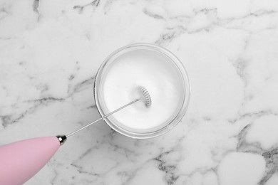 Photo of Mini mixer (milk frother) and whipped milk in glass on white marble table, top view