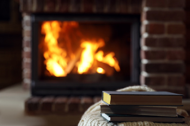 Books on table near burning fireplace, space for text. Reading at home