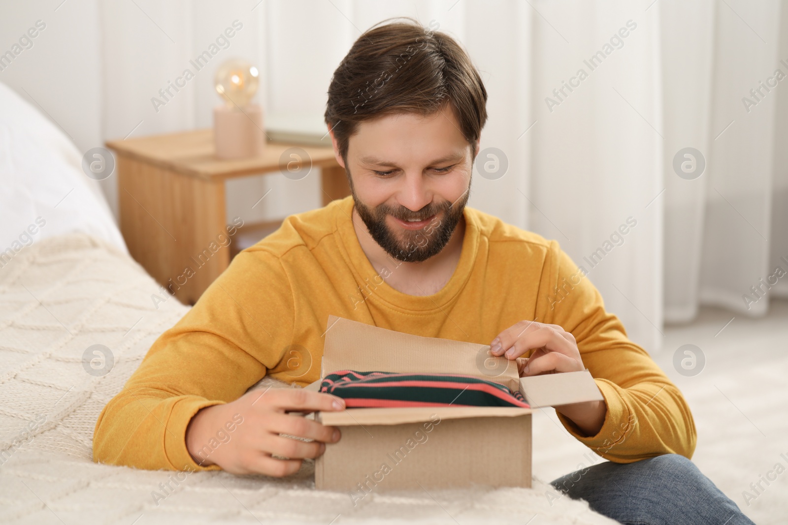 Photo of Happy man opening parcel at home. Internet shopping