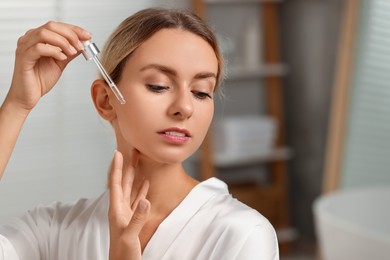 Beautiful woman applying cosmetic serum onto her face in bathroom, space for text