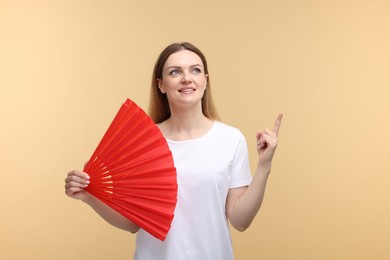 Happy woman with red hand fan pointing on beige background