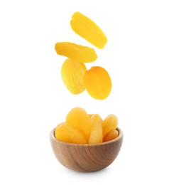 Tasty dried apricots falling into bowl on white background