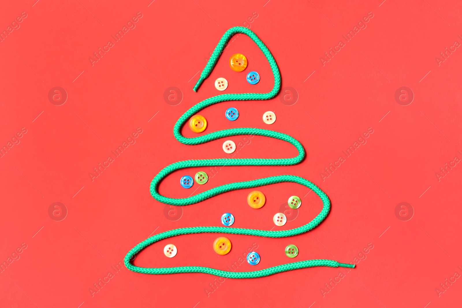 Photo of Christmas tree made of shoe lace and different buttons on red background, flat lay