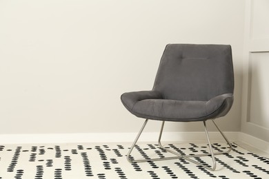 Stylish grey armchair near light wall in room. Space for text