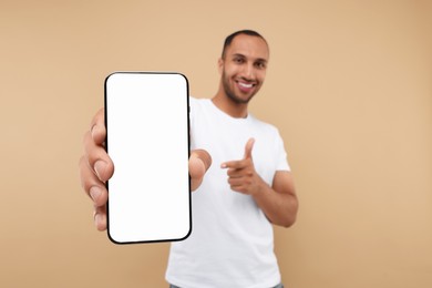 Young man showing smartphone in hand and pointing at it on beige background, selective focus. Mockup for design