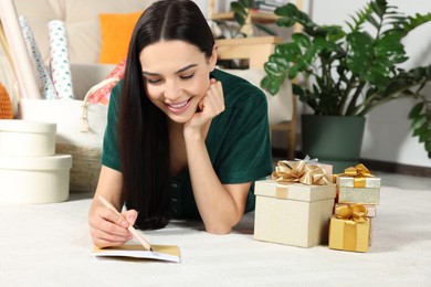 Photo of Happy woman writing message in greeting card on floor in living room