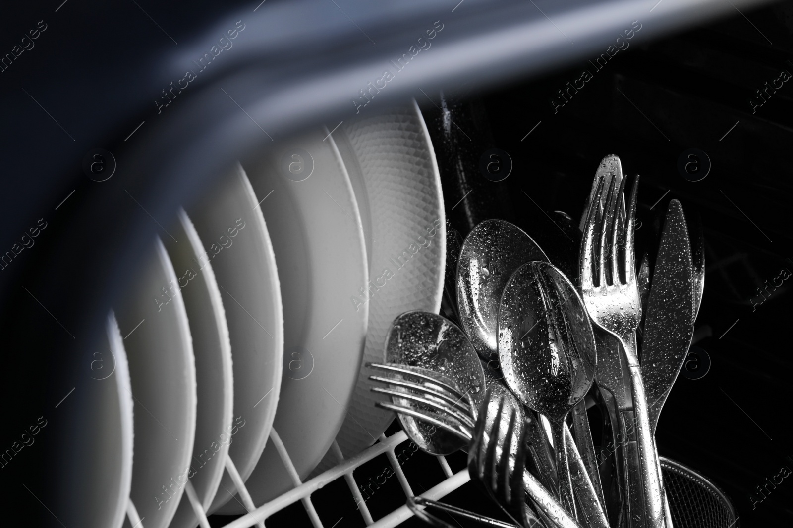 Photo of Clean wet plates and cutlery in dishwasher, closeup