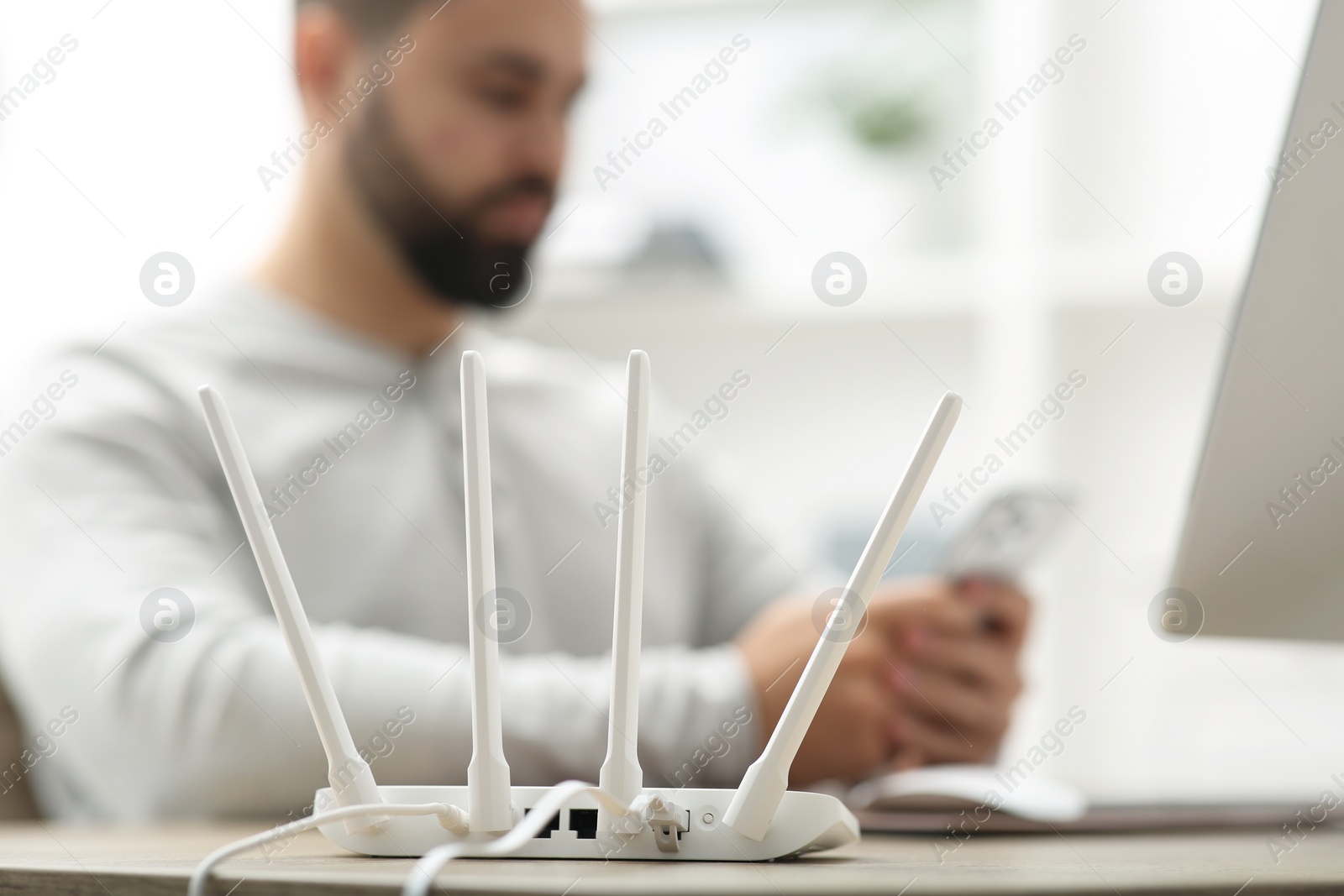 Photo of Man with smartphone working at wooden table indoors, focus on Wi-Fi router