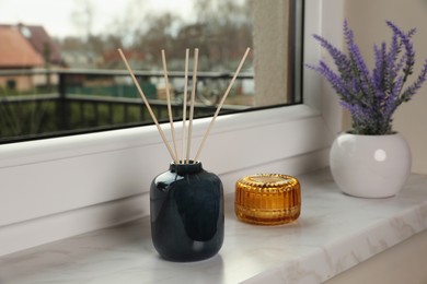 Aromatic reed air freshener, scented candle and lavender flowers on windowsill indoors