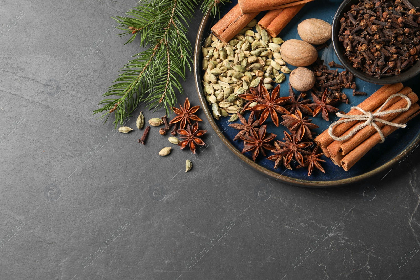 Photo of Dishware with different spices, nuts and fir branches on gray table, flat lay. Space for text