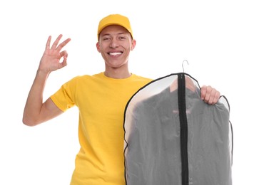 Photo of Dry-cleaning delivery. Happy courier holding garment cover with clothes and showing OK gesture on white background