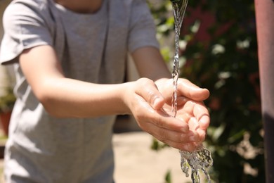 Photo of Water scarcity. Little boy drawing water with hands from tap outdoors, closeup