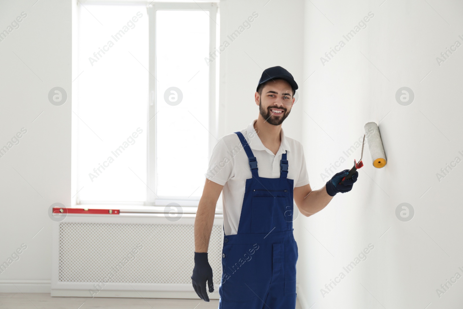 Photo of Handyman painting wall with roller brush indoors, space for text. Professional construction tools