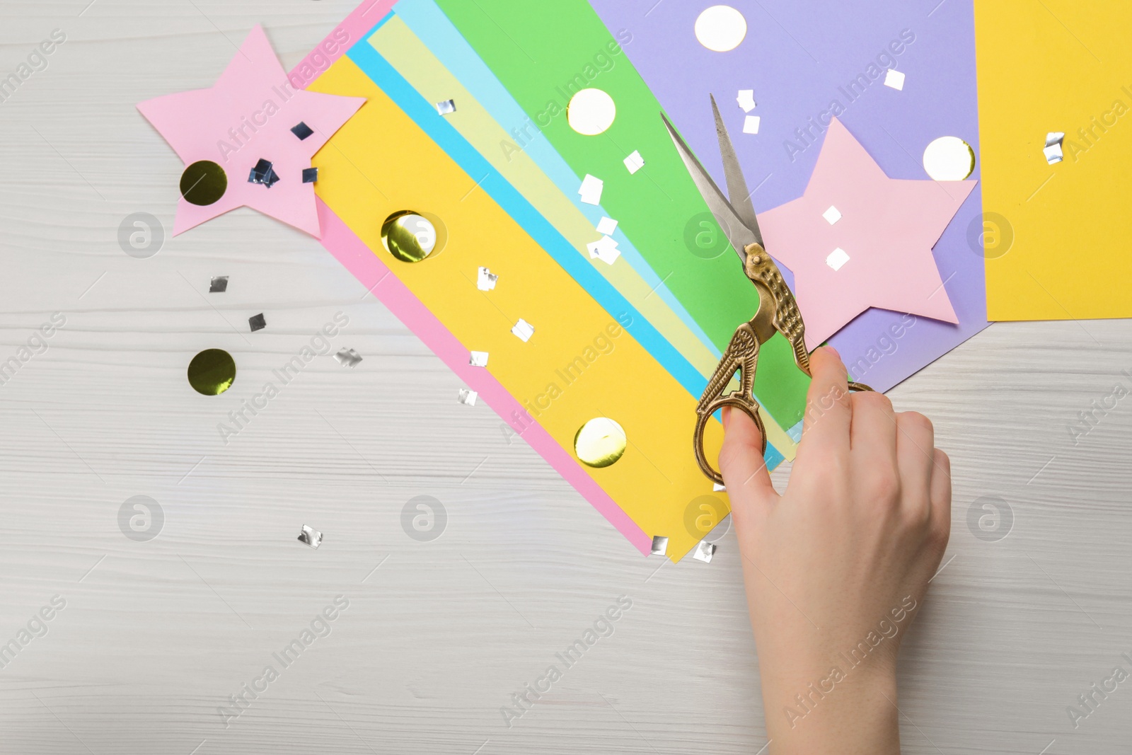 Photo of Woman holding scissors and colorful paper at white wooden table, top view. Space for text