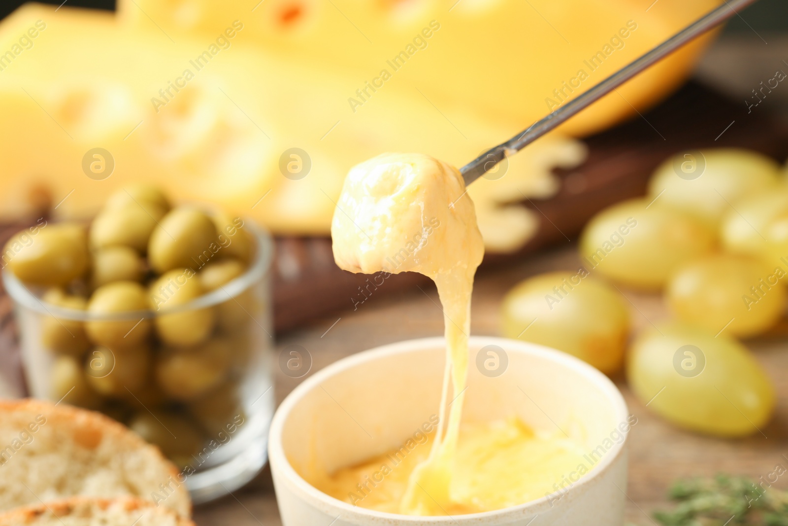 Photo of Piece of bread over bowl with delicious cheese fondue on wooden table