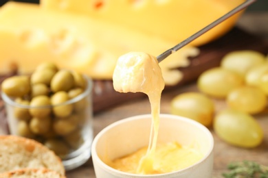 Photo of Piece of bread over bowl with delicious cheese fondue on wooden table