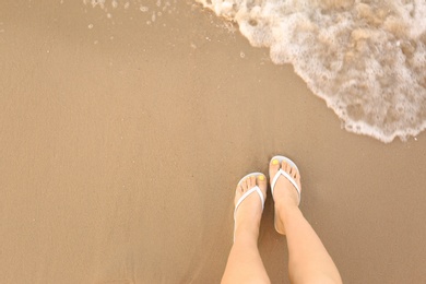 Photo of Top view of woman with white flip flops on sand near sea, space for text. Beach accessories