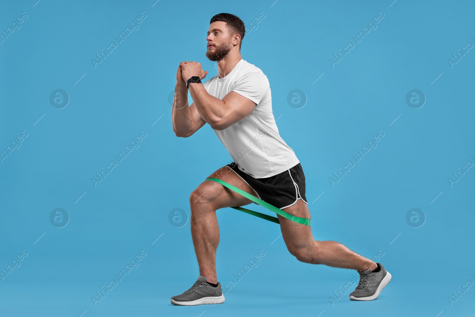 Photo of Young man exercising with elastic resistance band on light blue background