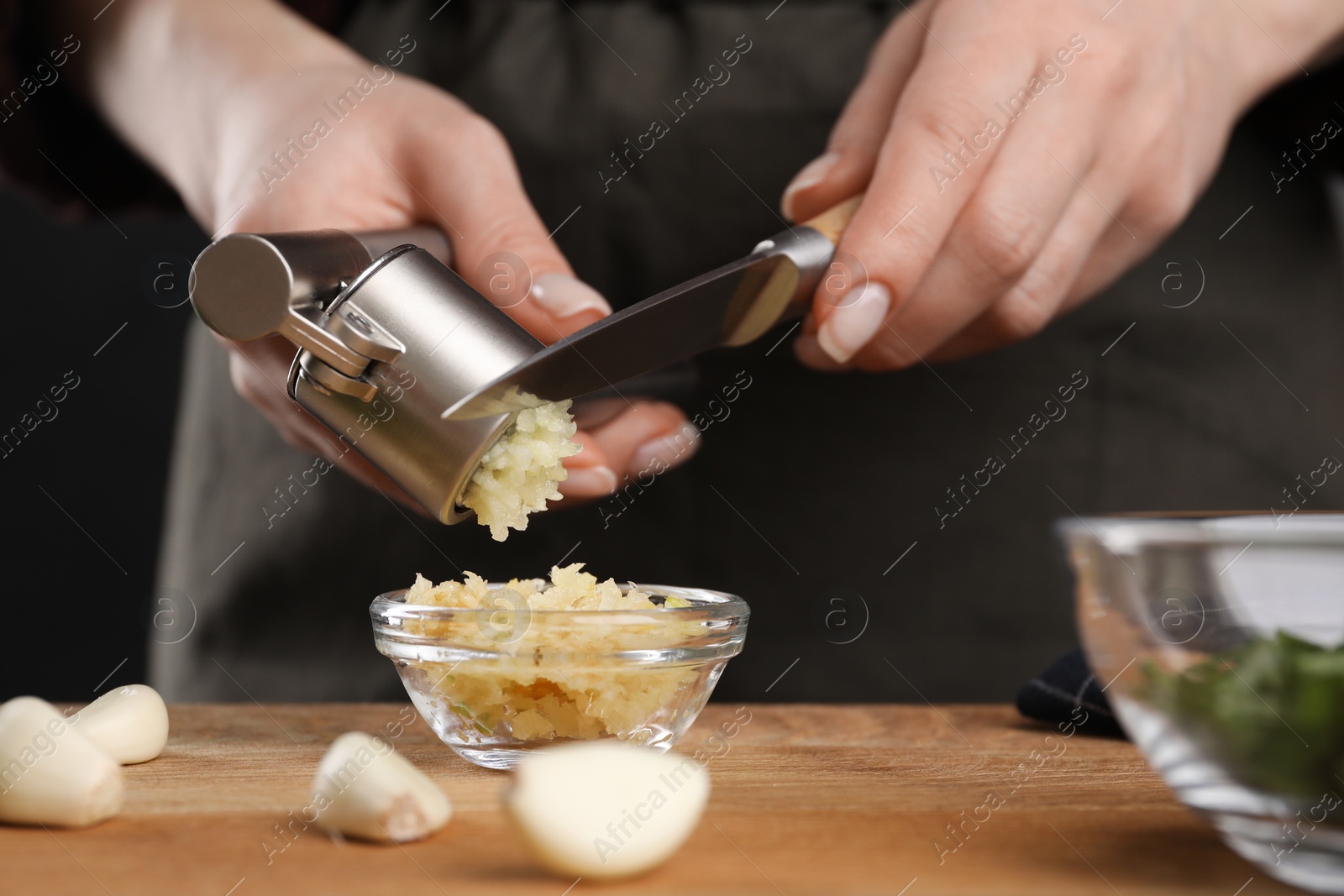 Photo of Woman squeezing garlic with press at wooden table, closeup