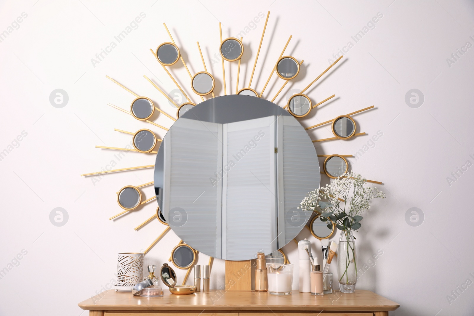 Photo of Dressing table with round mirror and cosmetic products near white wall. Interior element