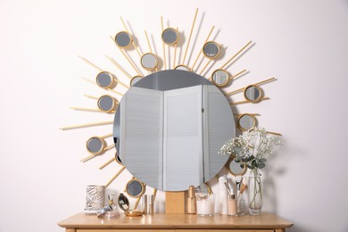 Dressing table with round mirror and cosmetic products near white wall. Interior element