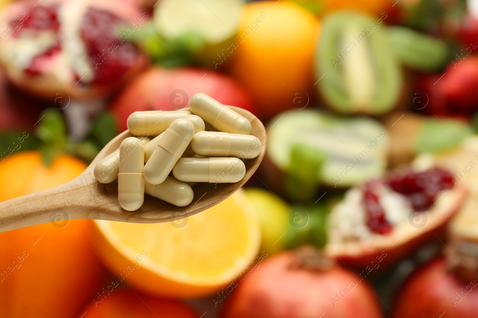 Photo of Vitamin pills in spoon against fresh fruits, closeup. Space for text