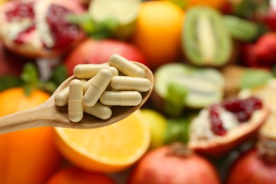 Photo of Vitamin pills in spoon against fresh fruits, closeup. Space for text