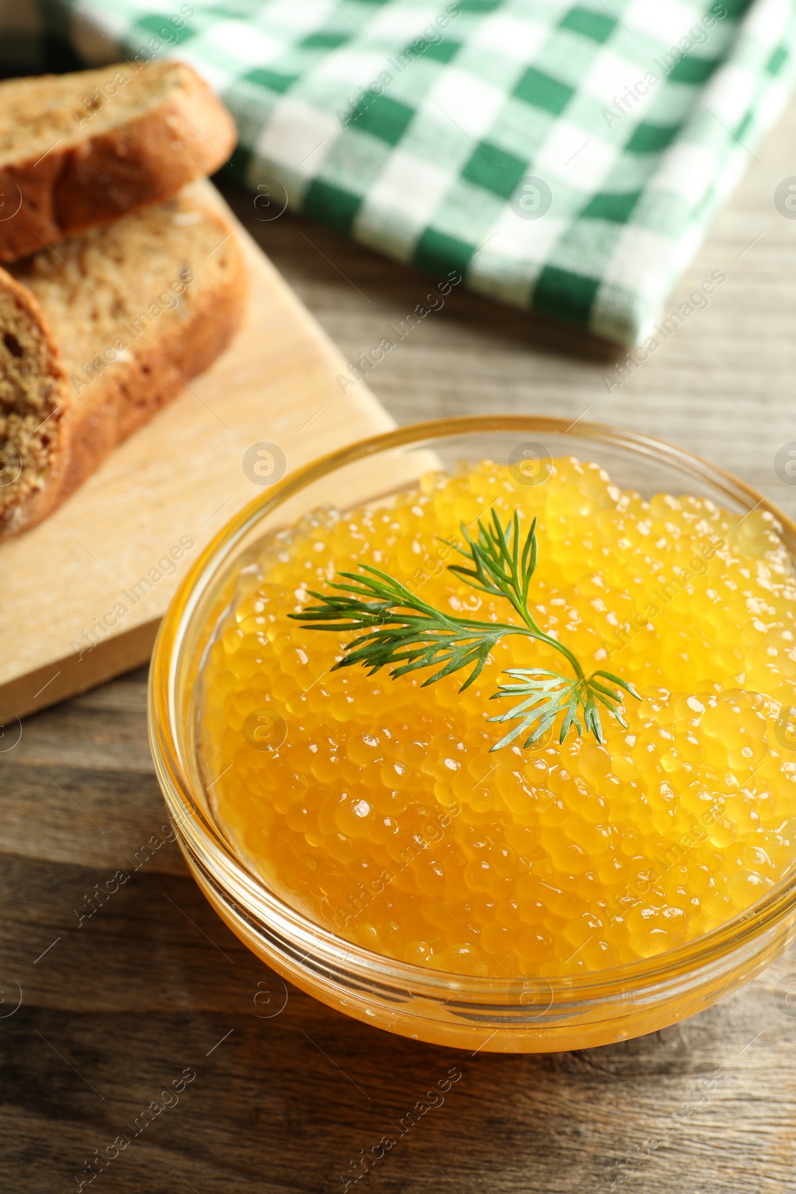 Photo of Fresh pike caviar in bowl and bread on wooden table, closeup